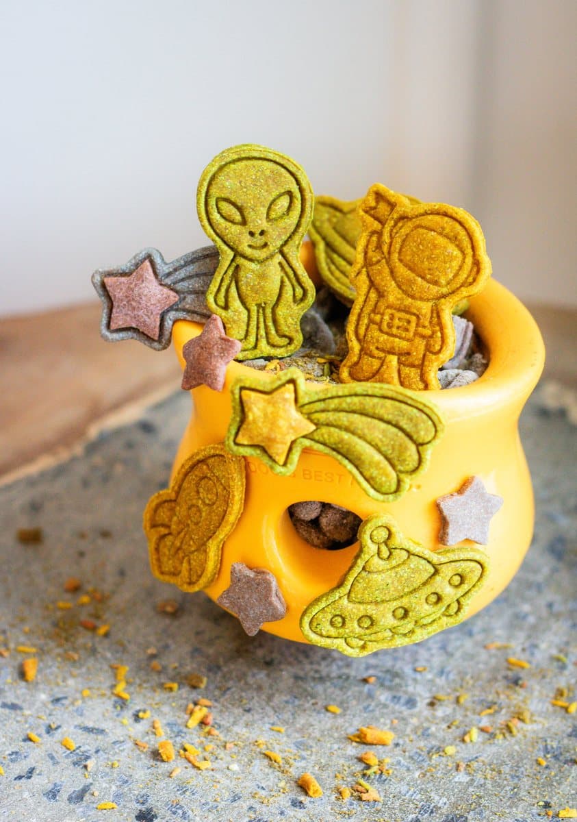 Biscuits pour chiens thématiques : un astronaute, un extraterrestre et des étoiles filantes débordant d'un bol orange
